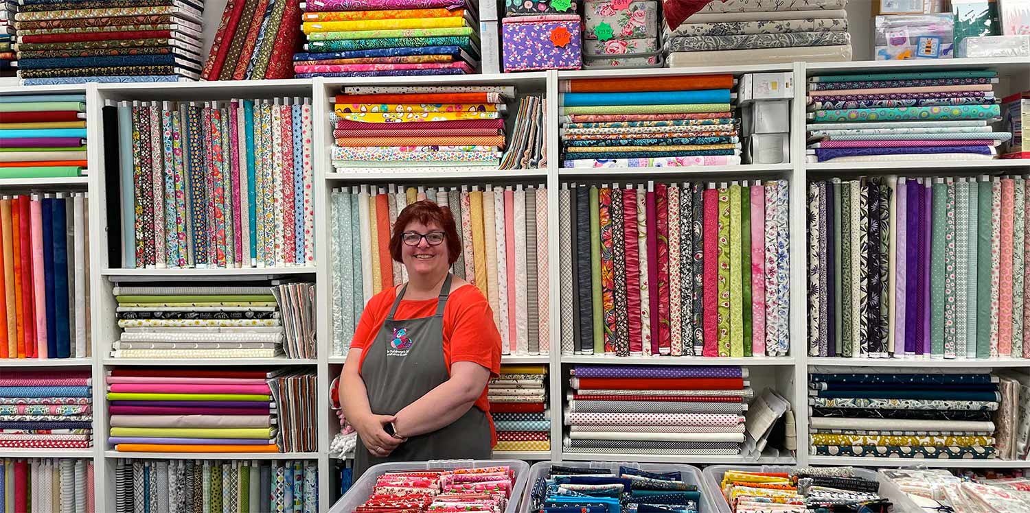 Sara Williams owner Patchwork Cat standing in front of hundreds of rolls of fabrics